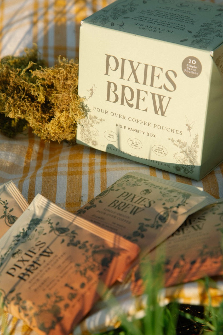 Box of Pixies Brew coffee pouches on a checkered tablecloth with greenery.