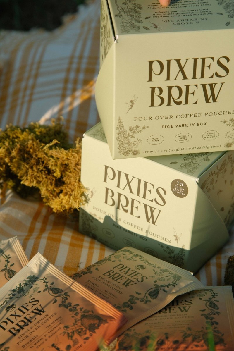 A Pixies Brew pour-over pouch brewing into a glass server at a golden-hour picnic